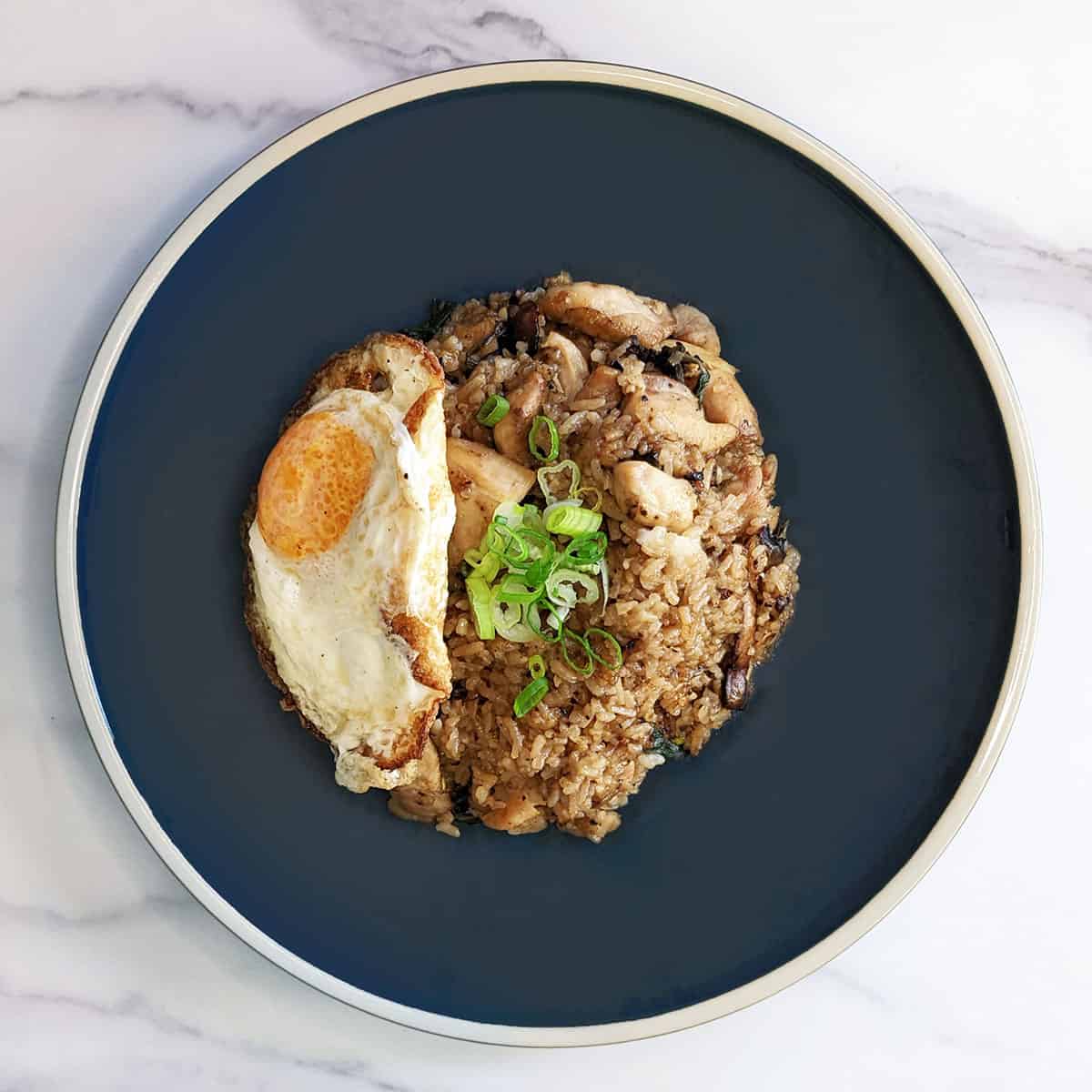 A blue plate with Thai basil chicken fried rice and a fried egg on top of a marble countertop