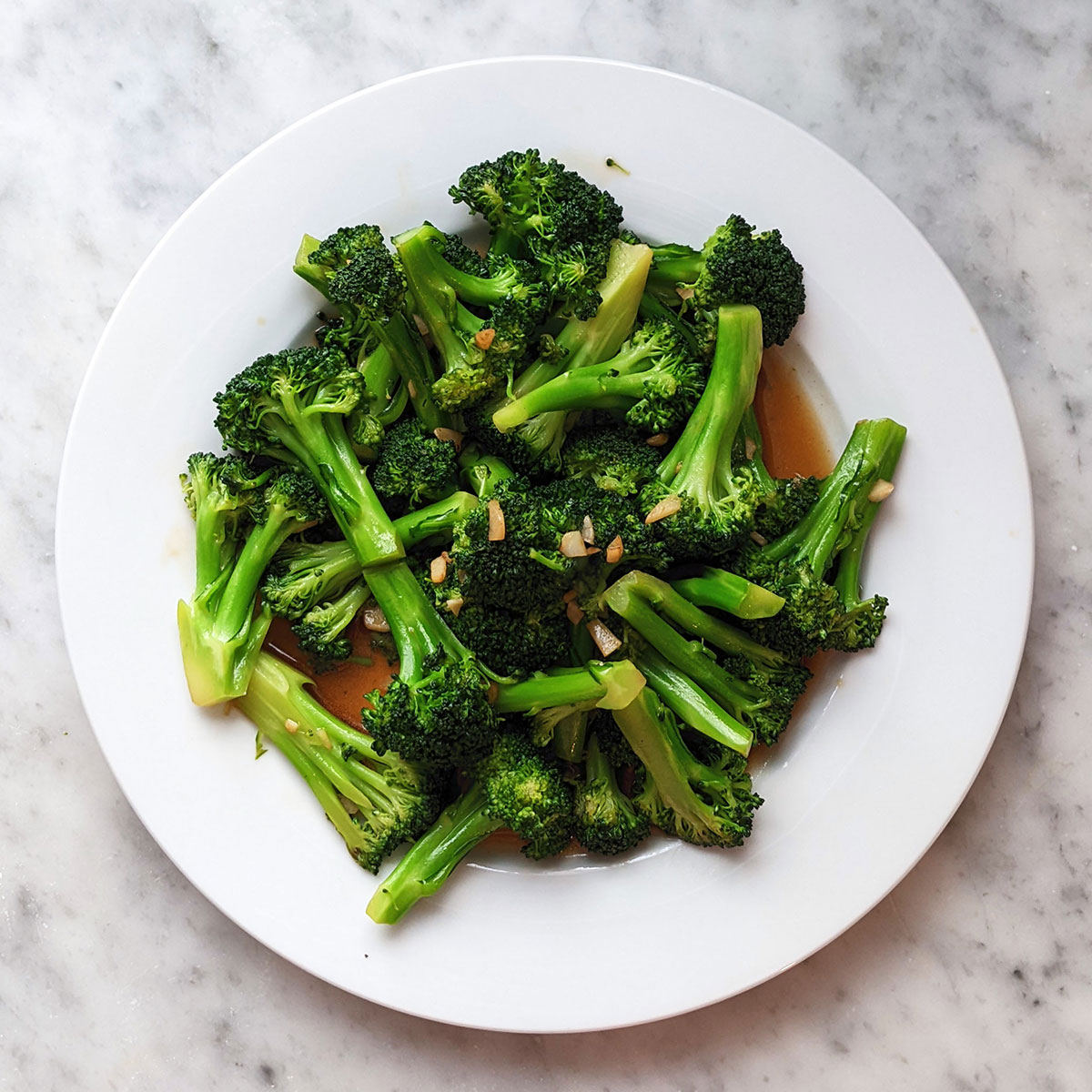 A plate of broccoli stir-fry with garlic on top of a marble backdrop