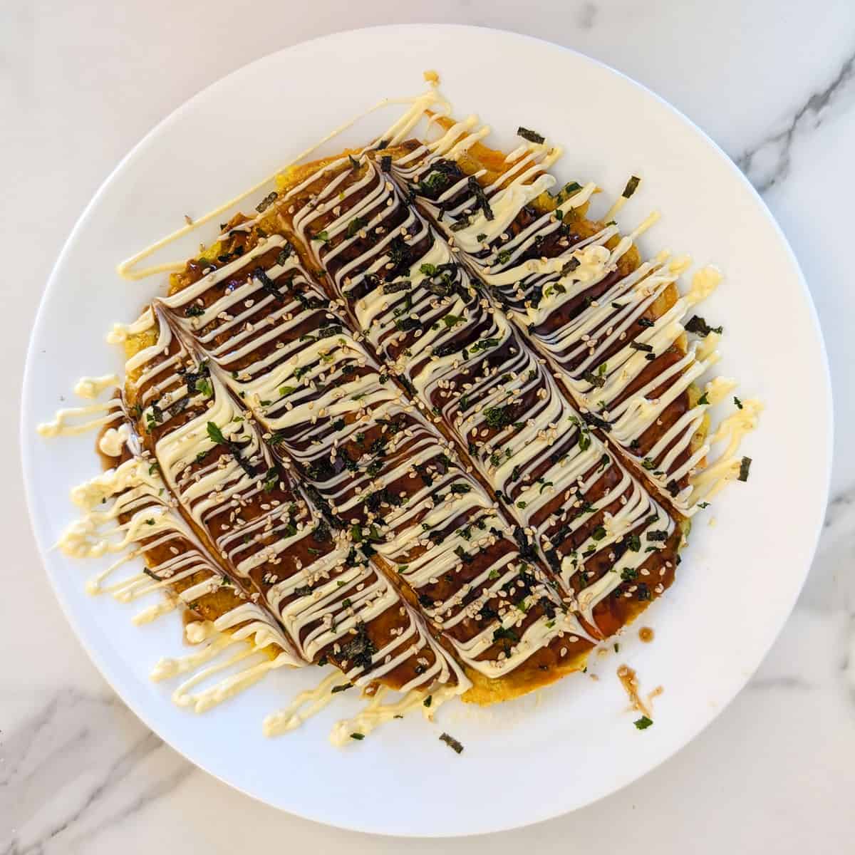 A plate of okonomiyaki on a white marble background