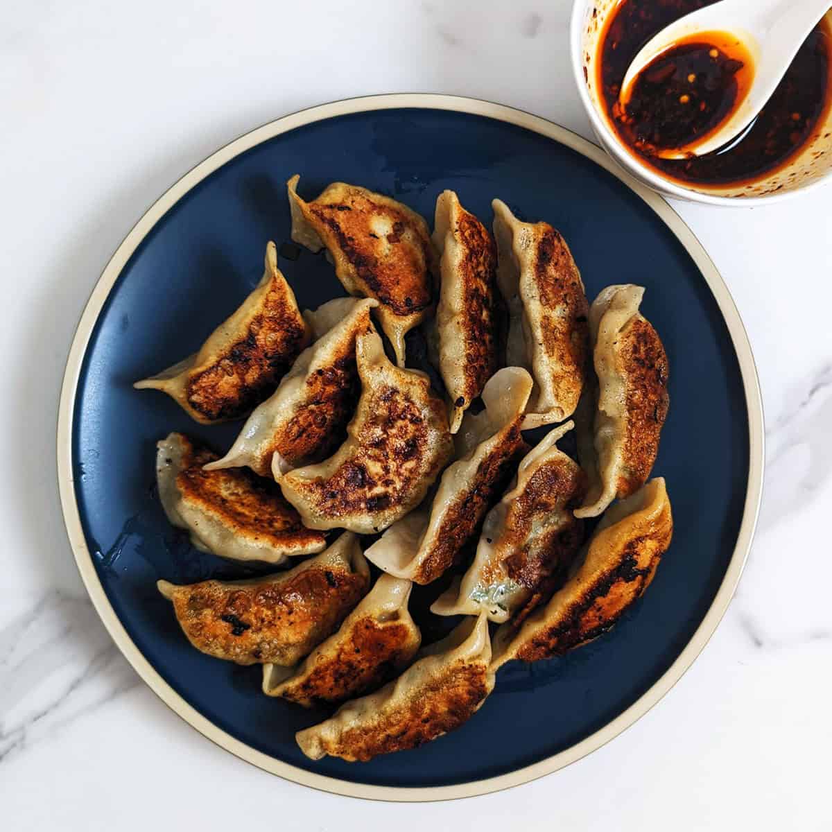 Image of pan-fried dumplings and a side of chili oil dipping sauce