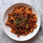 plate of noodles cooked in red chili oil topped with ground pork and chopped scallions