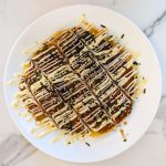 A plate of okonomiyaki on a white marble background